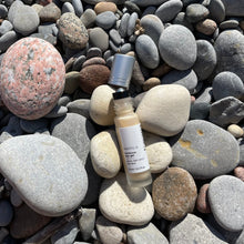 Load image into Gallery viewer, Kavana's Phyto-5 Luminous Eye Gel, is seen here opened, with roller ball top showing and cap just off the bottle to the right , on a bed of stones at the beach. Packed with Green Coffee extract to depuff, Hyaluronic Acid to hdyrate, Blue Cornflower to soothe and a mica blend to hilight, this is the cooling eye gel you need! It also has Kavana's signature Phyto-5 plant blend of Calendula, COmfrey, Echinacea, Plantain and Rosehip seed oil. Delighftul as a 2-in-1 multipurpose skincare and makeup product!