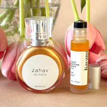 Load image into Gallery viewer, Kavana's Zahav EAu fraiche, golden shimmer spray for hair and decolletage, stands alongside Kavana's Neroli Calm Roll on aromatherapeutic perfume roll on. it also has a golden peach hue, that shimmers when applied on skin. Rose tulips in the background, fall over the ledge of a vase.