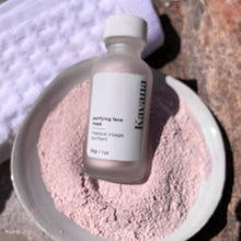Load image into Gallery viewer, Kavana's Purifying powder mask, is seen here: a 1oz./30ml. frosted clear glass bottle with a white cap, tilted into a ceramic ivory coloured bowl filled with the mask powder. Another bottle is in the background and a white, folded waffle towel is to the left, under the bottle that is tilting over into the bowl of powder.