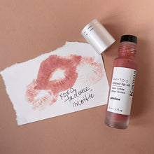 Load image into Gallery viewer, Kavana's Phyto-5 Tinted Lip Treatment Oil in Praline, a soft shade of rosy brown, THE perfect neutral for everyday wear. Seen here, the open roll on bottle with cap off, sits atop a love note that is signed 'xoxo, ta douce moitie', kisses from your better half.