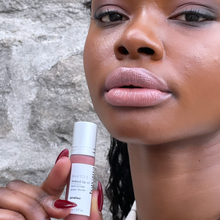 Load image into Gallery viewer, Model Raissa is seen holding a bottle of Kavana&#39;s Phyto-5 Tinted Lip Treatment oil in Praline. She is wearing Praline on her lips too- a sheer browny rose tinted lip oil.
