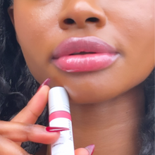 Load image into Gallery viewer, Model Raissa&#39;s lips are seen here in tight close up- she is holding up a bottle of Kavana&#39;s Phyto-5 TInted lip oil in Capucine, wearing it on her lips as well. A rich, true coral- it looks amazing on her!
