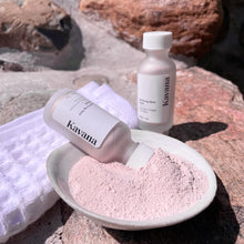 Load image into Gallery viewer, Kavana&#39;s Purifying powder mask, is seen here: a 1oz./30ml. frosted clear glass bottle with a white cap, tilted into a ceramic ivory coloured bowl filled with the mask powder. Another bottle is in the background and a white, folded waffle towel is to the left, under the bottle that is tilting over into the bowl of powder.
