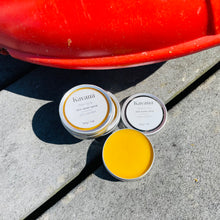 Load image into Gallery viewer, Kavana&#39;s Phyto-5 skin saver salve is perfect for late summer.  This bright yellow salve is excellent post bug bites or other broken skin. Pictured, the bright yellow salve in an open tin, with two propped salves, against a rescue buoy on a deck, with trees in the background.
