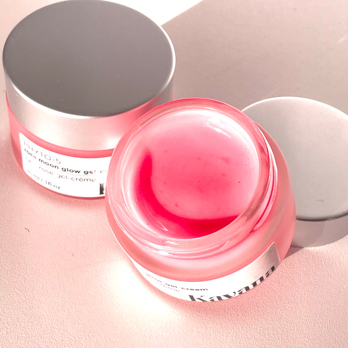 Rose Moon Glow Gel Cream is a lightweight primer and moisturizer, 2-in-1. Pictured here, the open jar with a brushed, matte silver coloured cap, perched on the lip of the jar. Another jar flipped on it's side, cane be seen, the pink colour of the gel showing through it. This gel goes on clear on the skin, leaving now colour behind. 