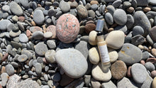 Load image into Gallery viewer, Kavana&#39;s Phyto-5 Luminous Eye Gel, is seen here opened, with roller ball top showing and cap just off the bottle to the right , on a bed of stones at the beach. Packed with Green Coffee extract to depuff, Hyaluronic Acid to hdyrate, Blue Cornflower to soothe and a mica blend to hilight, this is the cooling eye gel you need! It also has Kavana&#39;s signature Phyto-5 plant blend of Calendula, COmfrey, Echinacea, Plantain and Rosehip seed oil. Delighftul as a 2-in-1 multipurpose skincare and makeup product!
