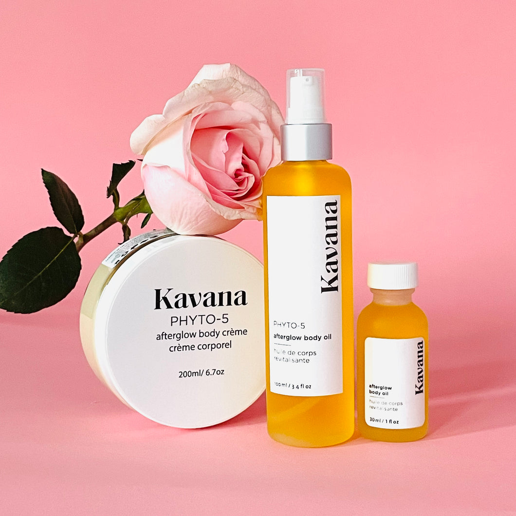 Kavana's Afterglow trio is plant powered body care at it's finest. Pictured, our mini travel size body oil, large body oil and large Body Cream, arranged side by side with a pale pink rose resting on the body cream, which is upright. The best of non-toxic, plant powered, hormones safe body care, with Kavana. 