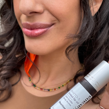 Load image into Gallery viewer, Model Kristel is seen in tight close up- lips only, and foreground is a frosted glass bottle w silver cap on, of Kavana&#39;s PHyto-5 TInted lip treatment oil in Libertine. A dark blackberry shade.
