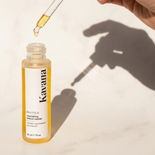 Load image into Gallery viewer, Kavana Bottle with dropper being pressed by a finger held in a hand we only see the shadow of. The oil is a golden yellow colour thanks to the rich plant profle of the oils inside, including Sea Buckthorn seed oil, Rosehip seed oil, 8 different essential oils to help balance the skin, including Niaouli, Rose, Lavender and more. 

