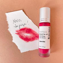 Load image into Gallery viewer, Kavana&#39;s Phyto-5 Tinted Lip Treatment oil in shade Capucine, a bright, summery coral, is seen closed here, overtop of a love note that says &#39;xoxo, ta puce&#39;. French for hugs and kisses, your love bug.
